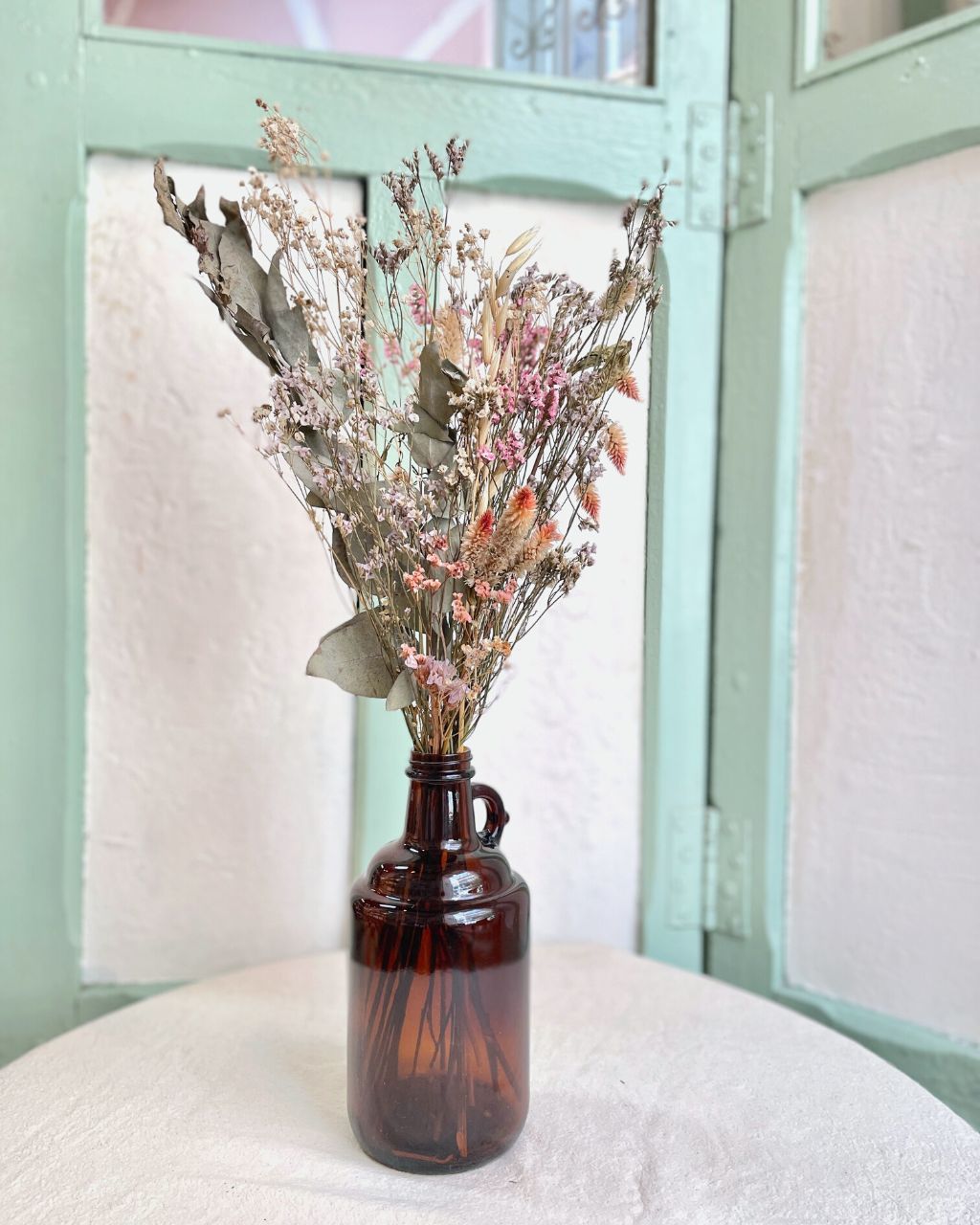 Arreglo de flores secas en botella en diseño ámbar para decorar espacios.