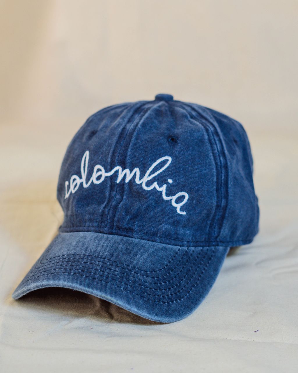 Gorra azul con letras blancas en cursiva que contiene la palabra Colombia.