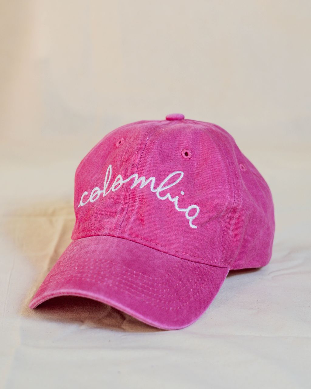 Gorra fucsia con letras blancas en cursiva que contiene la palabra Colombia.