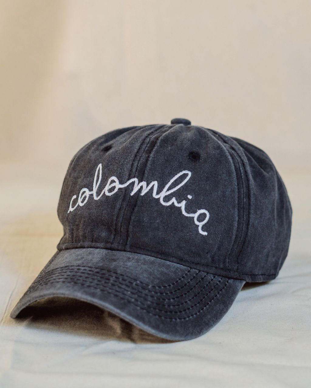 Gorra negra con letras blancas en cursiva que contiene la palabra Colombia.