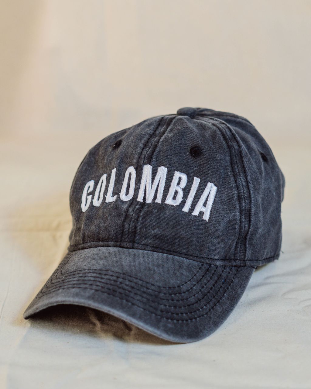 Gorra negra con letras blancas en mayúscula que contiene la palabra Colombia.